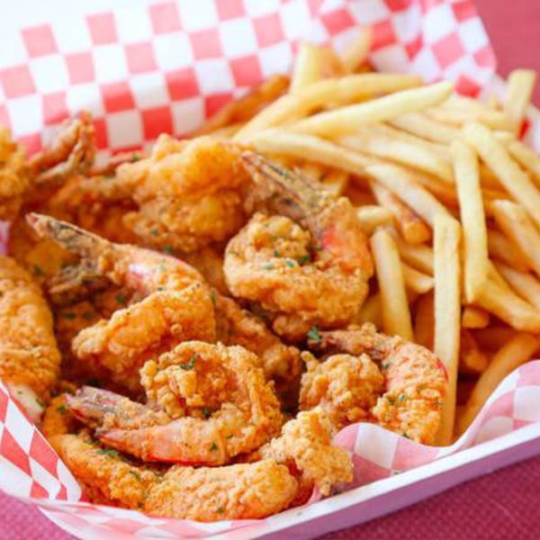Crispy fried shrimp and golden french fries served in a red and white checkered paper tray.
