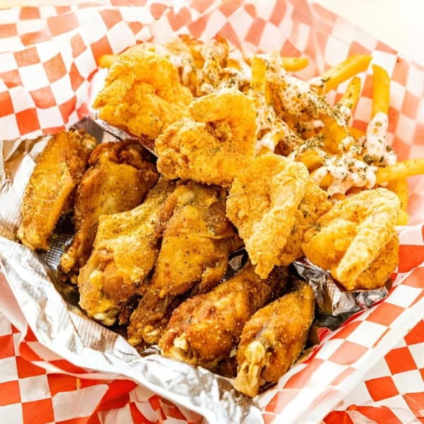 Le Roux's Chicken Shack fried chicken wings, tenders, and seasoned fries in a red checkered basket.