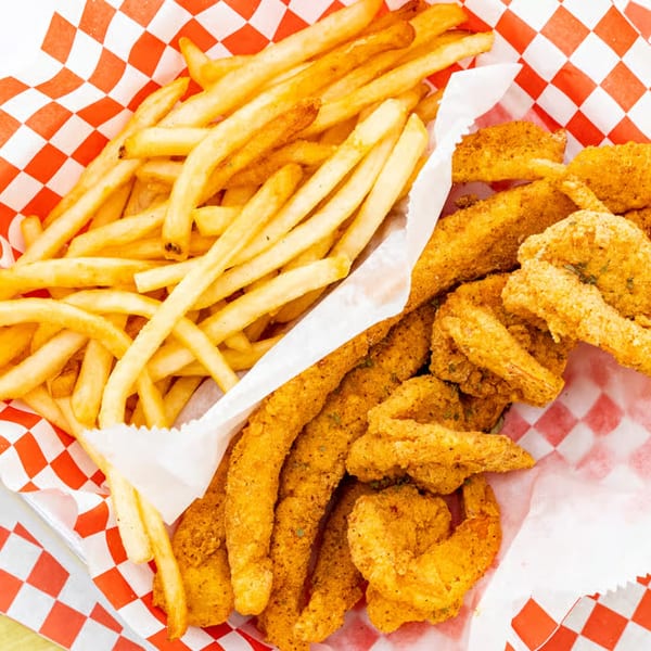 Le Roux's Chicken Shack fried chicken strips and shrimp with french fries in a red checkered basket.
